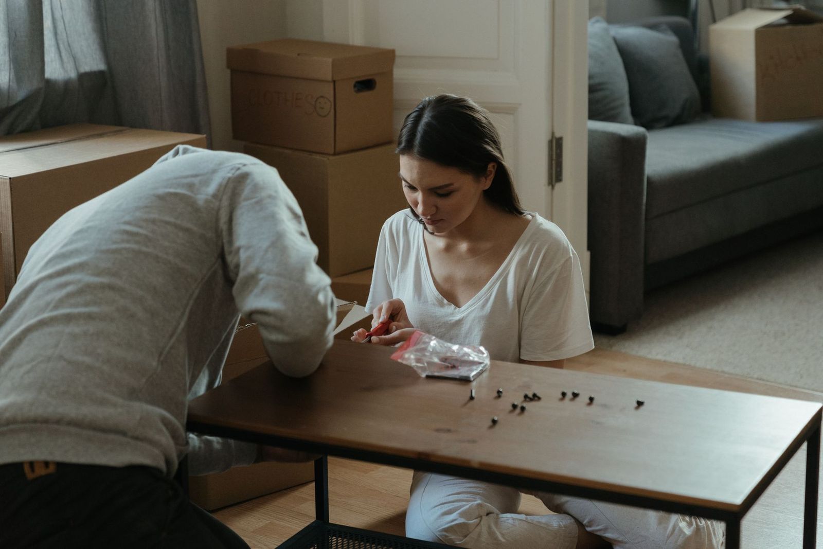 Paar baut in der neuen Wohnung zwischen Umzugskartons einen Couchtisch zusammen